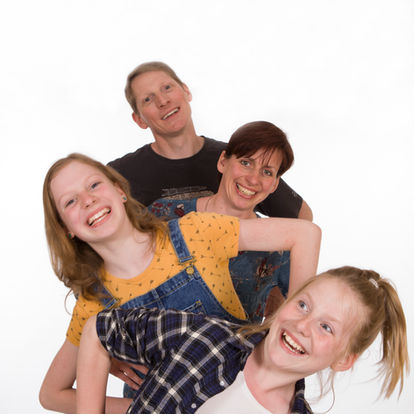 Four people, two adults and two children, stand in a staggered line, smiling and leaning playfully against each other against a plain white background. Andy Boyle Photography