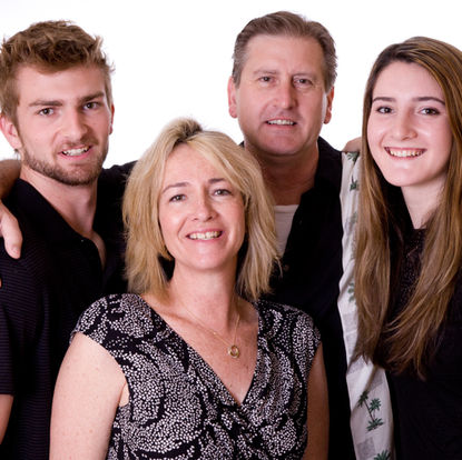 Four people, two men and two women, stand closely together smiling at the camera against a plain white background. Andy Boyle Photography