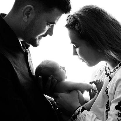 Black and white photo of a man and woman holding a newborn baby, facing each other closely and gazing at the infant. Andy Boyle Photography