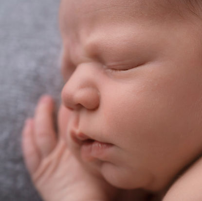 Close-up of a newborn baby sleeping with eyes closed, lying on their side with one hand resting near the face. Andy Boyle Photography