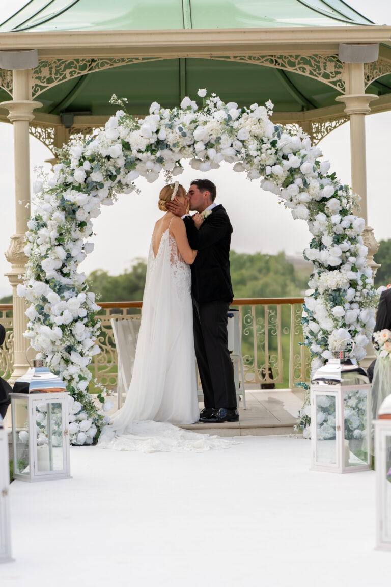 Bride and groom kissing under floral arch.